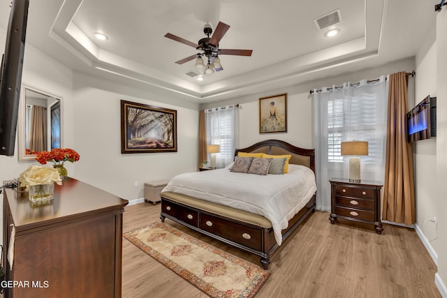 bedroom with visible vents, a raised ceiling, light wood finished floors, and baseboards