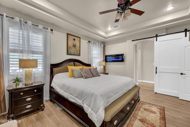 bedroom featuring a tray ceiling, light wood-type flooring, a barn door, and visible vents