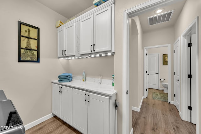 laundry area featuring visible vents, light wood finished floors, and baseboards