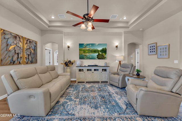 living room featuring arched walkways, ceiling fan, visible vents, and a raised ceiling