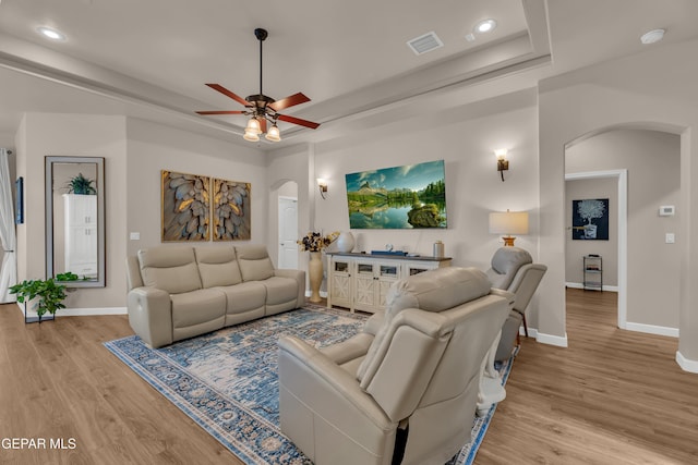 living area with visible vents, arched walkways, a raised ceiling, and light wood-style flooring