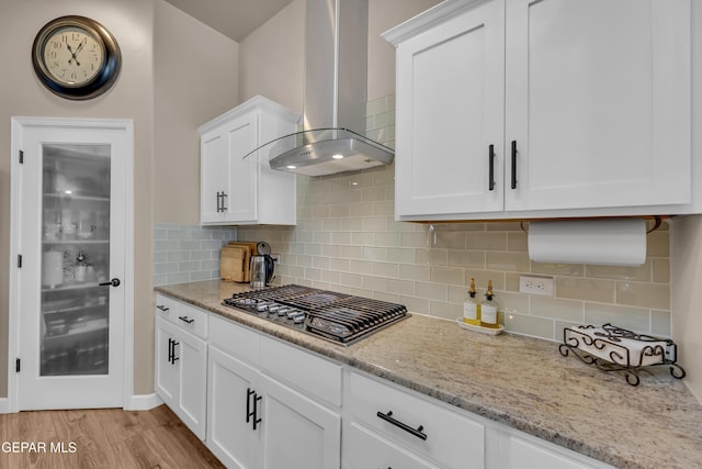 kitchen with wall chimney range hood, stainless steel gas cooktop, light stone counters, and light wood-style floors