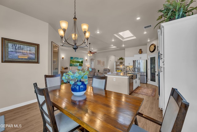 dining space with visible vents, recessed lighting, light wood finished floors, ceiling fan with notable chandelier, and a skylight