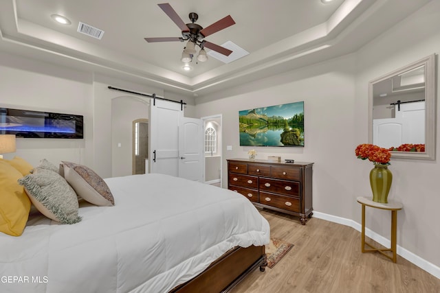 bedroom featuring light wood-style floors, baseboards, recessed lighting, a barn door, and a tray ceiling