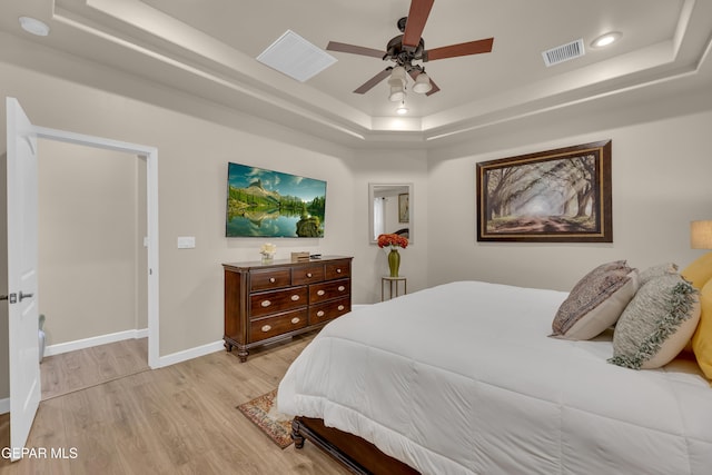 bedroom featuring light wood-style floors, a raised ceiling, baseboards, and visible vents