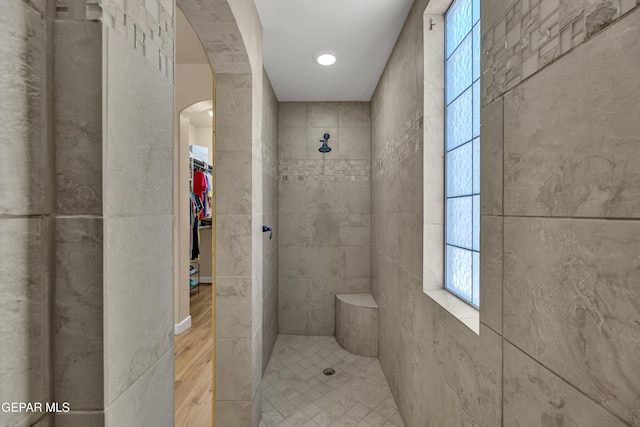 bathroom featuring a walk in closet, wood finished floors, and a tile shower