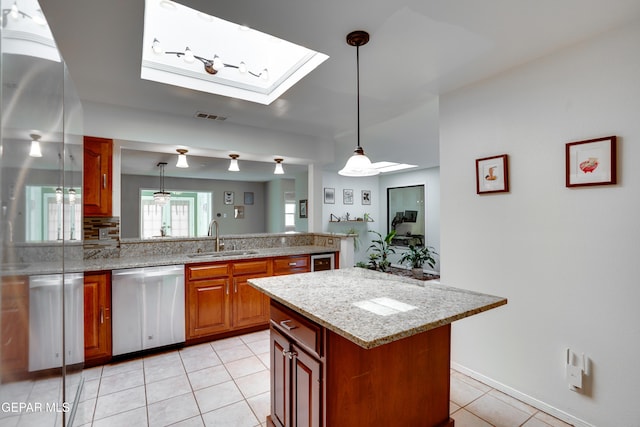 98 Northwind Dr, El Paso, TX 79912 - kitchen featuring stainless steel dishwasher, a sink, light tile patterned floors, brown cabinetry, and a skylight