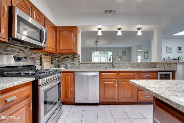 98 Northwind Dr, El Paso, TX 79912 - kitchen with stainless steel appliances, a sink, brown cabinets, and tasteful backsplash