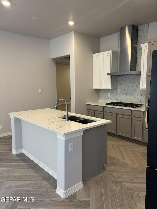kitchen featuring wall chimney exhaust hood, appliances with stainless steel finishes, baseboards, an island with sink, and backsplash