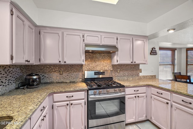 kitchen with under cabinet range hood, decorative backsplash, stainless steel gas range, and light stone counters
