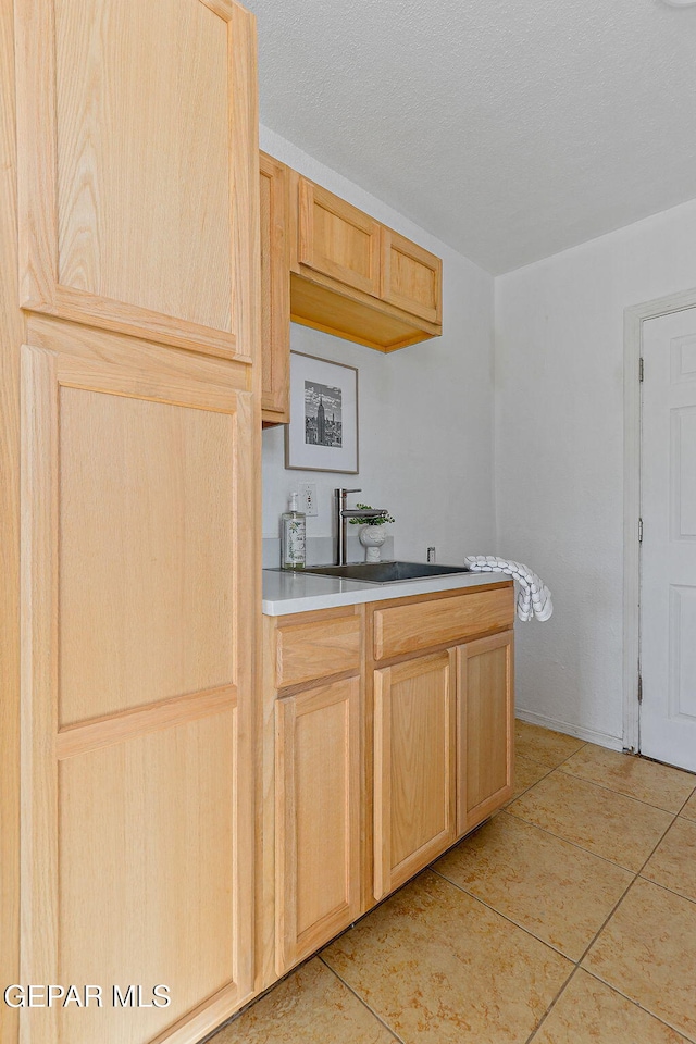 kitchen with light brown cabinetry, a sink, light tile patterned floors, and light countertops
