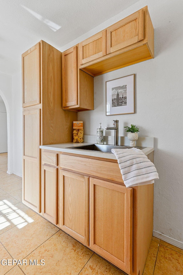 kitchen featuring a sink, arched walkways, light countertops, and light tile patterned floors