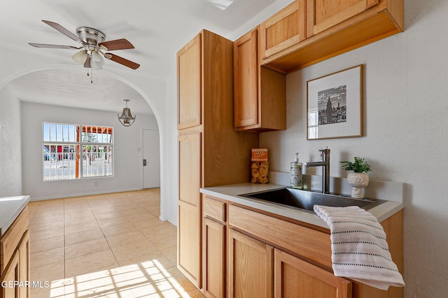 kitchen featuring arched walkways, a ceiling fan, light countertops, a sink, and light tile patterned floors