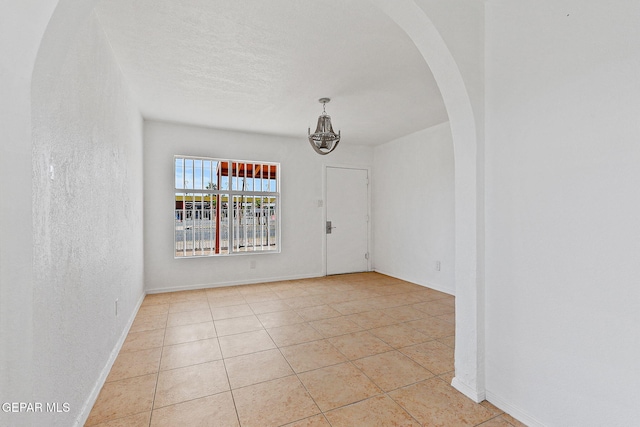 spare room featuring arched walkways, light tile patterned floors, and baseboards
