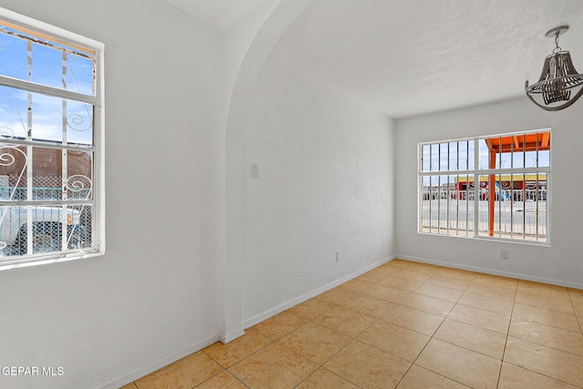spare room featuring tile patterned floors, baseboards, and arched walkways
