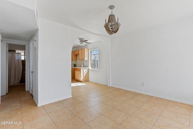 empty room with a chandelier, light tile patterned flooring, ceiling fan, arched walkways, and baseboards