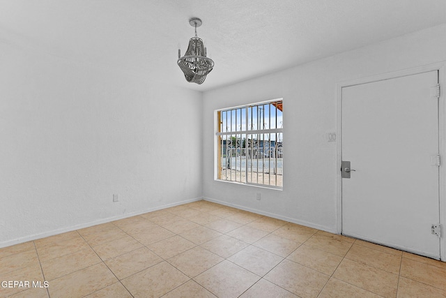 tiled empty room featuring a chandelier and baseboards