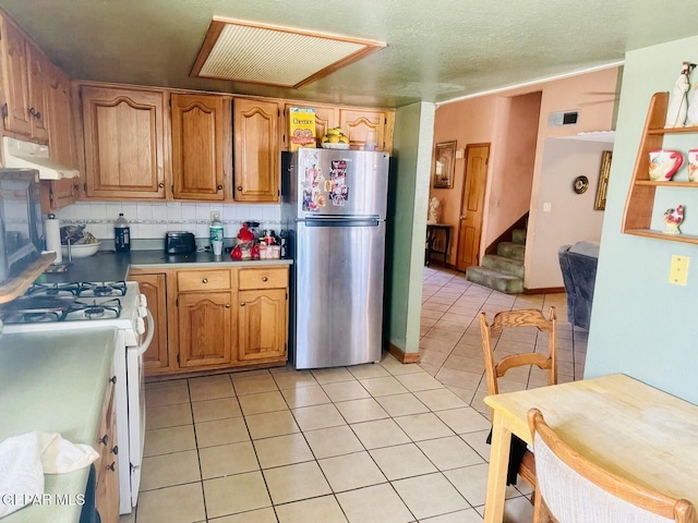 kitchen with light tile patterned floors, freestanding refrigerator, white gas range, visible vents, and under cabinet range hood