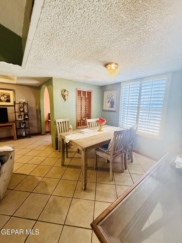 dining space featuring arched walkways, light tile patterned flooring, and a textured ceiling