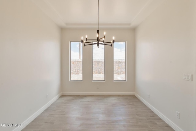 unfurnished room with a tray ceiling, light wood-style floors, baseboards, and a notable chandelier