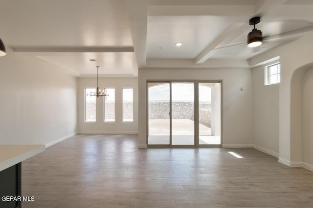 interior space with wood finished floors, baseboards, ceiling fan with notable chandelier, and beamed ceiling