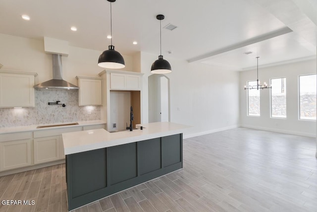kitchen featuring a sink, wall chimney exhaust hood, a notable chandelier, backsplash, and light countertops