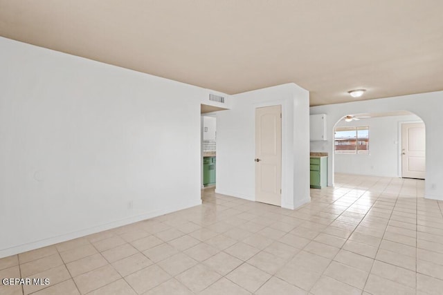 unfurnished room with light tile patterned floors, arched walkways, baseboards, and a ceiling fan