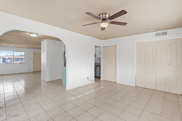 spare room with arched walkways, ceiling fan, light tile patterned floors, and baseboards