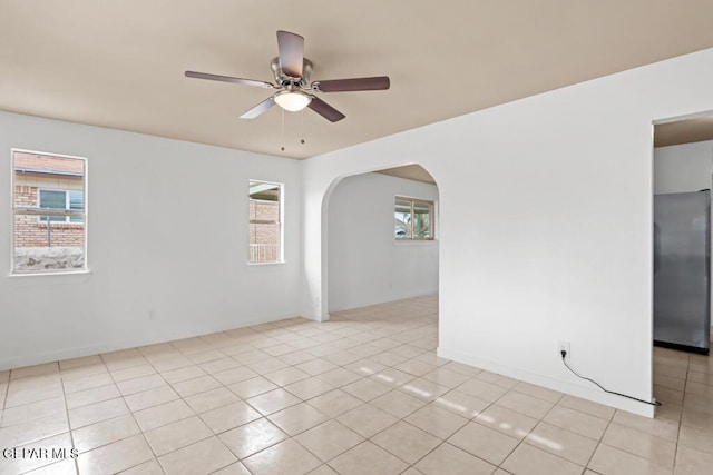 spare room featuring a ceiling fan, arched walkways, light tile patterned floors, and baseboards