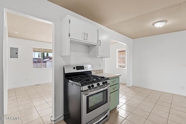 kitchen with stainless steel range with gas stovetop, light countertops, white cabinets, arched walkways, and light tile patterned floors