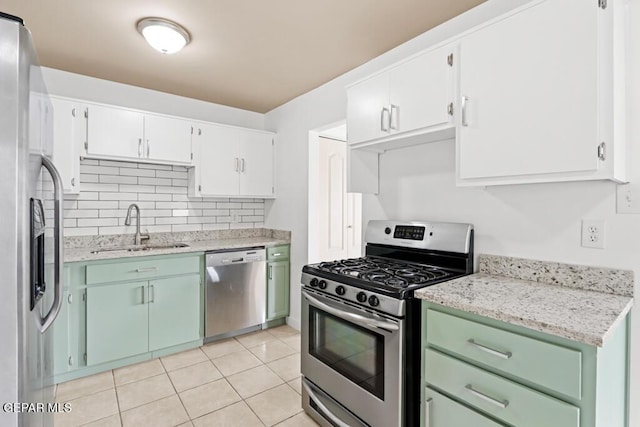 kitchen with appliances with stainless steel finishes, a sink, tasteful backsplash, light tile patterned floors, and white cabinets