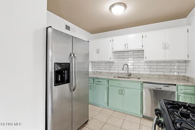 kitchen featuring a sink, stainless steel appliances, light tile patterned floors, tasteful backsplash, and white cabinetry