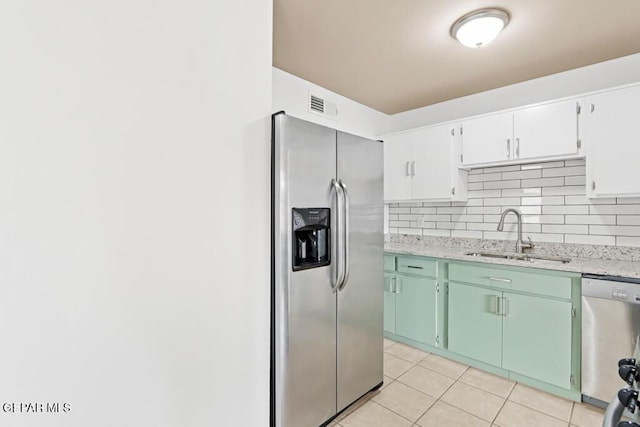 kitchen featuring stainless steel appliances, a sink, light tile patterned flooring, decorative backsplash, and white cabinets
