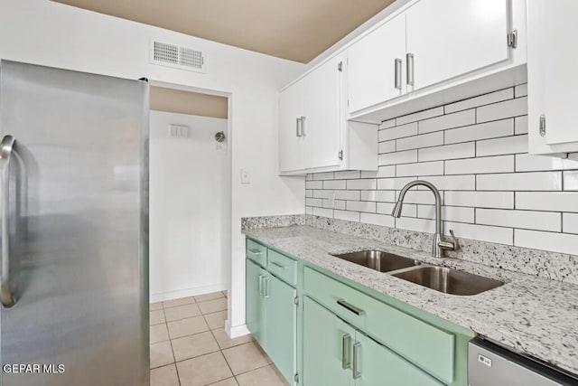kitchen with appliances with stainless steel finishes, a sink, white cabinetry, decorative backsplash, and light tile patterned flooring