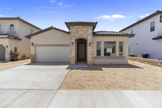 mediterranean / spanish-style house with an attached garage, stone siding, a tiled roof, stucco siding, and driveway