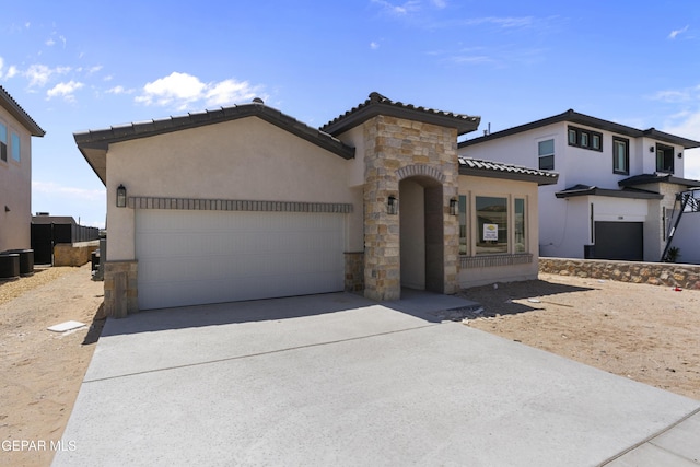 mediterranean / spanish home featuring an attached garage, stone siding, driveway, a tile roof, and stucco siding