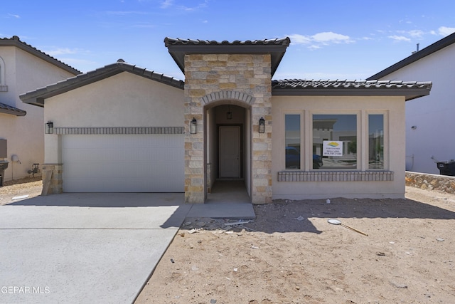 mediterranean / spanish-style house featuring stone siding, a garage, stucco siding, a tile roof, and concrete driveway