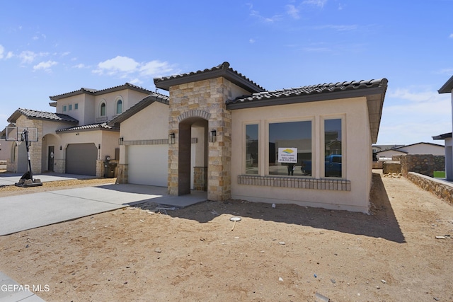 mediterranean / spanish-style home featuring an attached garage, stone siding, a tiled roof, stucco siding, and driveway