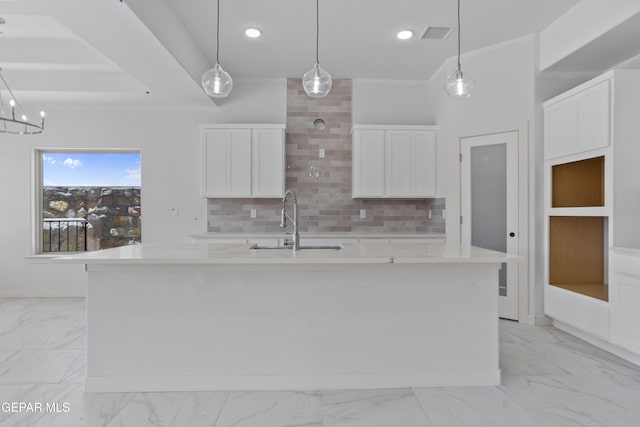 kitchen with an island with sink, a sink, white cabinetry, tasteful backsplash, and marble finish floor