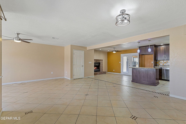 unfurnished living room with a ceiling fan, a textured ceiling, light tile patterned floors, baseboards, and a brick fireplace