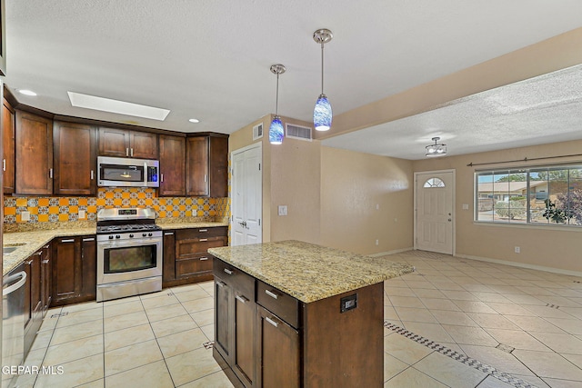kitchen featuring appliances with stainless steel finishes, light tile patterned floors, backsplash, light stone counters, and hanging light fixtures