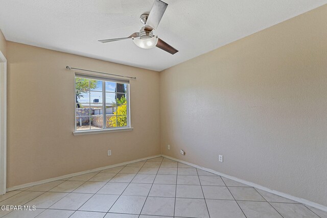 empty room with ceiling fan, light tile patterned floors, and baseboards