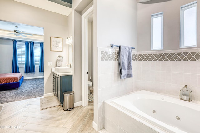 ensuite bathroom featuring a jetted tub, toilet, plenty of natural light, and a ceiling fan
