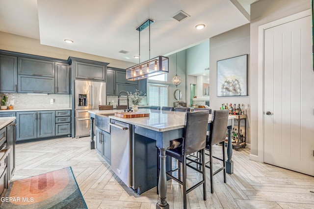 kitchen featuring appliances with stainless steel finishes, a breakfast bar, backsplash, decorative light fixtures, and light stone counters