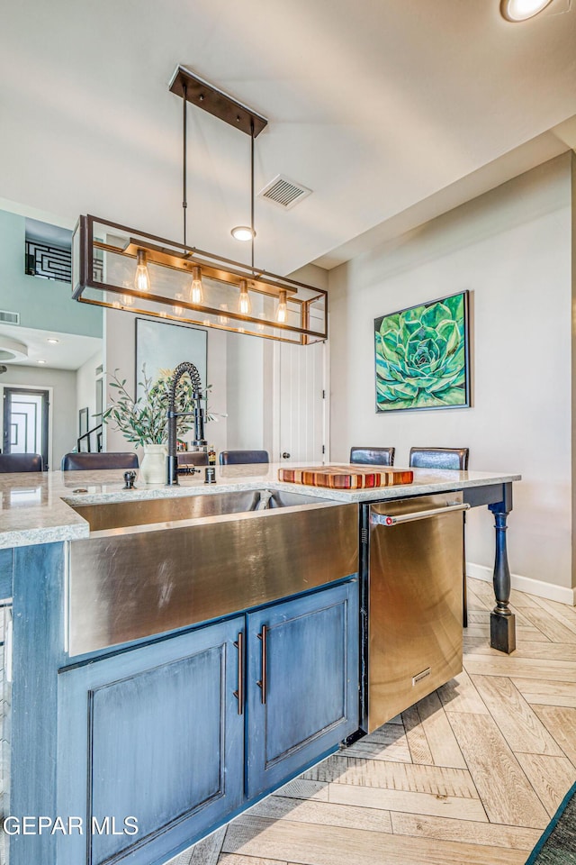 kitchen with dishwasher, a sink, blue cabinets, hanging light fixtures, and baseboards