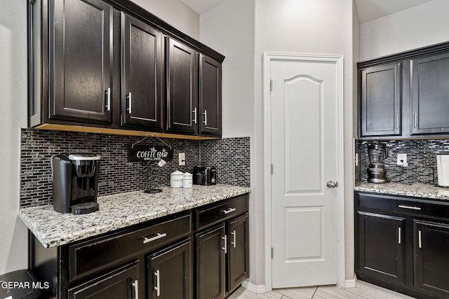 kitchen featuring decorative backsplash, light stone counters, and dark brown cabinets