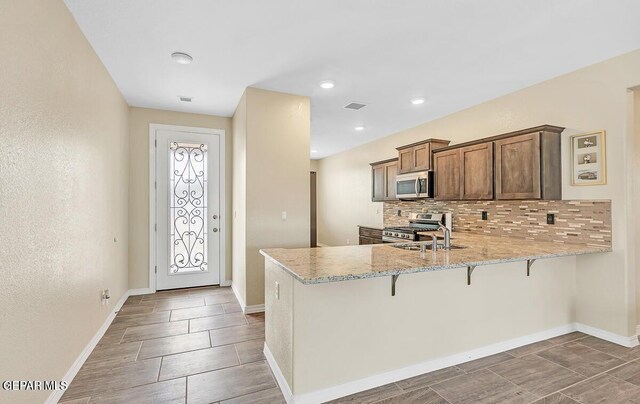 14920 Tierra Fortaleza Ave, El Paso, TX 79938 - kitchen with a peninsula, a breakfast bar area, stainless steel appliances, baseboards, and decorative backsplash