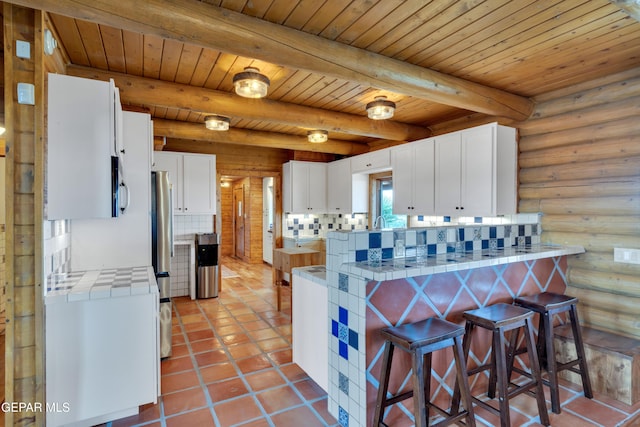 2 Scenic Ridge Rd N, Alpine, TX 99999 - kitchen featuring tile countertops, a peninsula, a breakfast bar, white cabinetry, and log walls