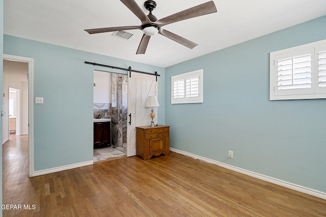 4731 Leeds Ave, El Paso, TX 79903 - unfurnished bedroom with a barn door, baseboards, ensuite bathroom, visible vents, and wood finished floors