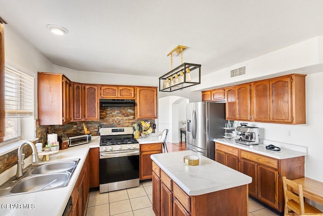 kitchen with stainless steel appliances, a sink, tasteful backsplash, arched walkways, and brown cabinetry